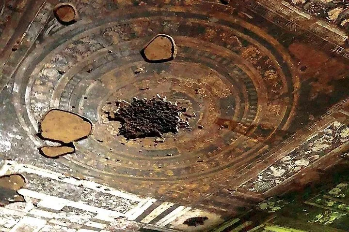 Damaged ceiling painting with intricate circular patterns and floral motifs at Ajanta Caves.