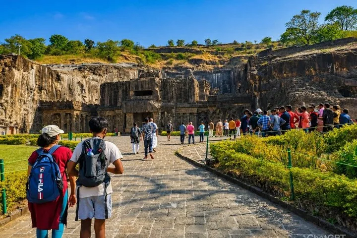 Tourists walking towards the impressive rock-cut facade of Ajanta Caves on a sunny day.