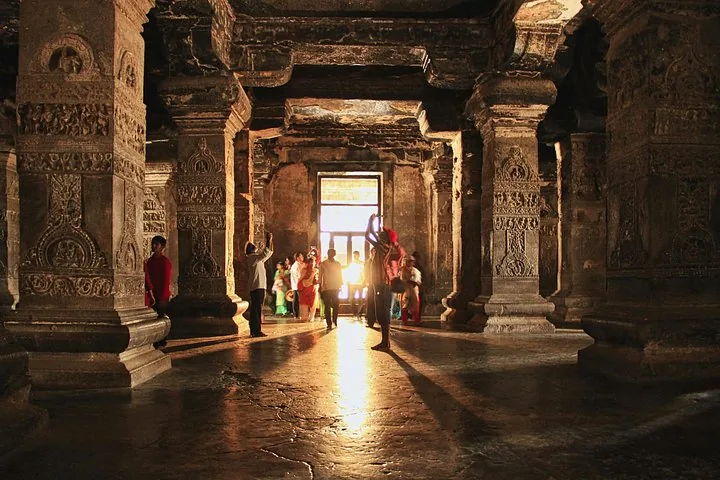 Tourists exploring the dimly lit, pillared interior of a cave at Ajanta Caves.